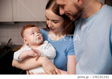 Loving family moment with parents and baby in cozy kitchen setting showcasing warmth, connection, and joy of parenthood, family bonding concept 136191242