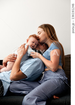 Loving family moment with parents embracing their baby while sitting on a couch, showcasing affection and connection in a cozy home environment, family bonding concept Loving family moment with parents embracing their baby while sitting on a couch, showcasing affection and connection in a cozy home environment, family bonding concept 136191246