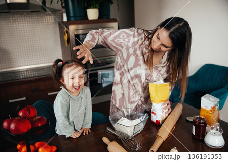 Young girl enjoys baking with mother in kitchen, laughing as they prepare ingredients for cookies on a weekend morning Young girl enjoys baking with mother in kitchen, laughing as they prepare ingredients for cookies on a weekend morning 136191353