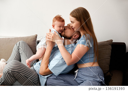 Loving family moment with parents and baby sharing joy and affection on a cozy couch in a bright living room healthy family concept 136191393