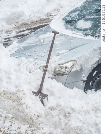Snow shoveling around a car parked on the street during winter weather in an urban area 136192115