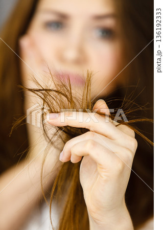 Worried woman looking at her dry hair ends Worried woman looking at her dry hair ends 136192333