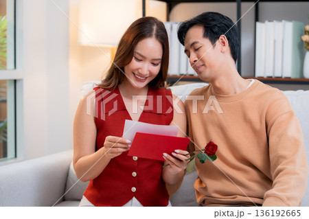 Happy asian couple sitting on sofa celebrating Valentine's Day with romantic surprise. 136192665