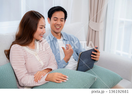 Happy asian couple video call on tablet together in living room at home. Happy asian couple video call on tablet together in living room at home. 136192681