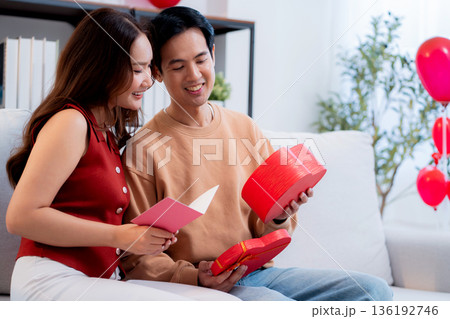 Asian young man and girlfriend celebrating Valentine's Day, woman holding card and gift box. Asian young man and girlfriend celebrating Valentine's Day, woman holding card and gift box. 136192746