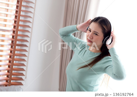 Happy young asian woman wearing headphones listening music while standing dancing with fun. 136192764