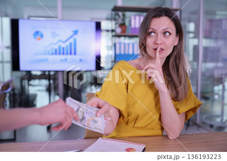 Businesswoman shares a secret while receiving cash in a bright office environment 136193223