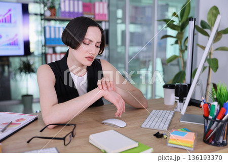 Busy office worker checks time while surrounded by colorful stationery and digital reports in a modern workspace Busy office worker checks time while surrounded by colorful stationery and digital reports in a modern workspace 136193370