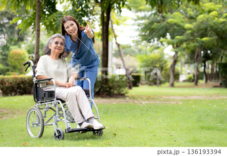 Young caucasian nurse comforting with patient while sitting on wheelchair in outdoor park. Young caucasian nurse comforting with patient while sitting on wheelchair in outdoor park. 136193394