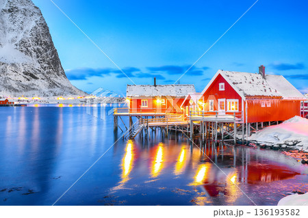 Outstanding evening cityscape of Reine town. Red rorbuers on the shoore of Reinefjorden. Outstanding evening cityscape of Reine town. Red rorbuers on the shoore of Reinefjorden. 136193582