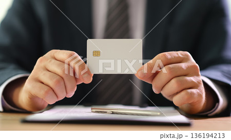 Business professional displaying a blank credit card against a modern office backdrop during a productive workday 136194213