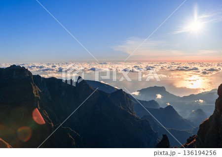 Colorful sunrise over Pico do Arieiro iconic ridge with sun rays lens flare and Atlantic clouds Colorful sunrise over Pico do Arieiro iconic ridge with sun rays lens flare and Atlantic clouds 136194256