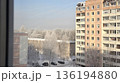 Winter city view from apartment window with residential buildings and snowy trees in morning light. 136194880