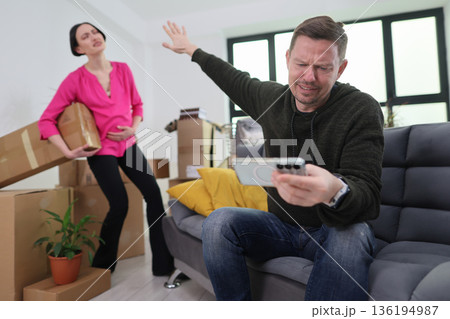 Emotional tension unfolds in a messy living room as a woman carries boxes while a man reacts to a phone call Emotional tension unfolds in a messy living room as a woman carries boxes while a man reacts to a phone call 136194987