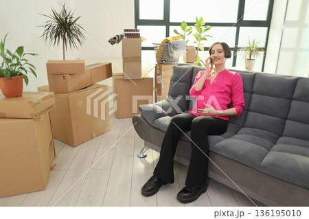 Excitement fills the air as a pregnant woman relaxes on her couch surrounded by moving boxes in her new home Excitement fills the air as a pregnant woman relaxes on her couch surrounded by moving boxes in her new home 136195010