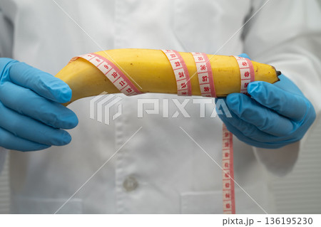 Doctor holding a banana with measuring tape, penis health. Doctor holding a banana with measuring tape, penis health. 136195230
