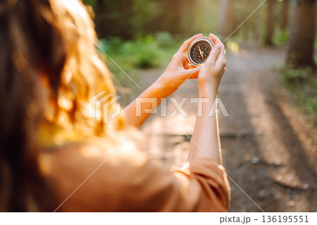 A hiker with curly hair holds a compass in their hands, carefully navigating through a sunlit forest A hiker with curly hair holds a compass in their hands, carefully navigating through a sunlit forest 136195551