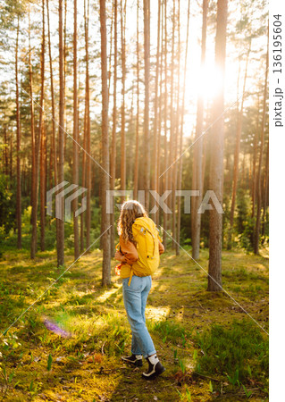 Tourist woman hiking alone in thick autumn forest. Stylish female looks for pathway among trees. 136195604