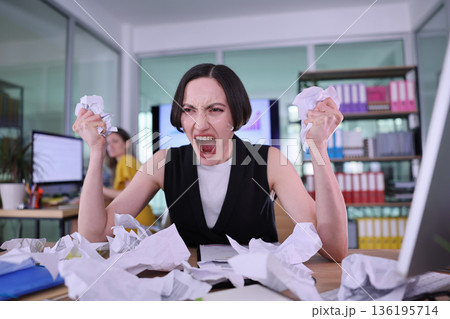 Frustration and chaos in a modern office as a woman expresses her emotions surrounded by crumpled papers Frustration and chaos in a modern office as a woman expresses her emotions surrounded by crumpled papers 136195714