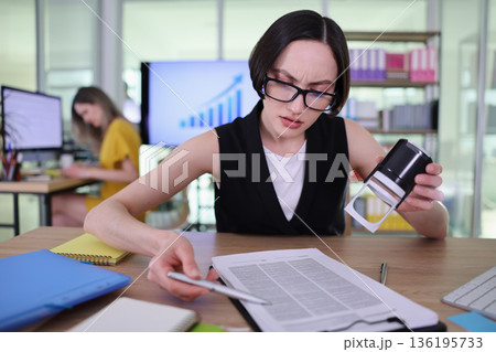 Busy professional reviews important documents while colleague works on a project in a modern office space during daytime 136195733