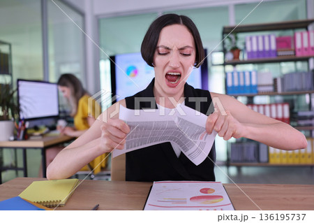 Frustration and determination collide as a woman tears a report in a bright, modern office space on a busy workday Frustration and determination collide as a woman tears a report in a bright, modern office space on a busy workday 136195737