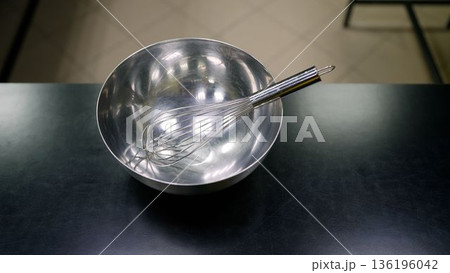 Stainless steel whisk resting in mixing bowl on table Stainless steel whisk resting in mixing bowl on table 136196042