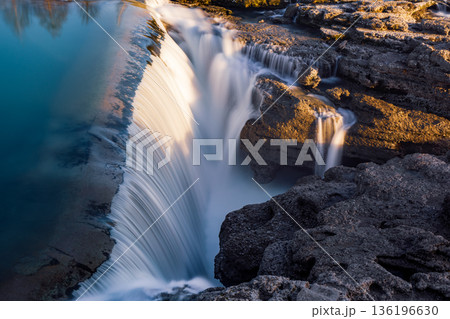 Golden Hour Waterfall Over Rugged Rocks Creates Serene Natural Landscape With Cascading Water 136196630