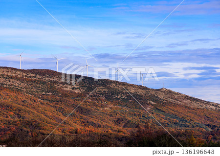 Autumn Hillside With Wind Turbines Under Blue Sky Over Colorful Foliage Landscape 136196648