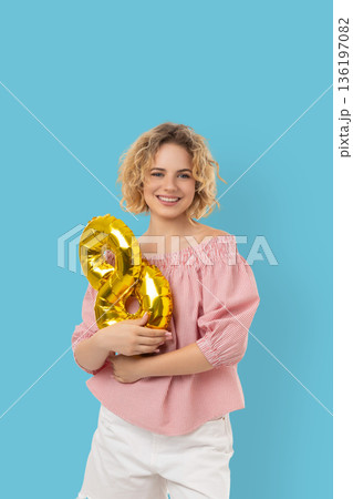 Woman smiles while holding gold balloons in the shape of eight Woman smiles while holding gold balloons in the shape of eight 136197082