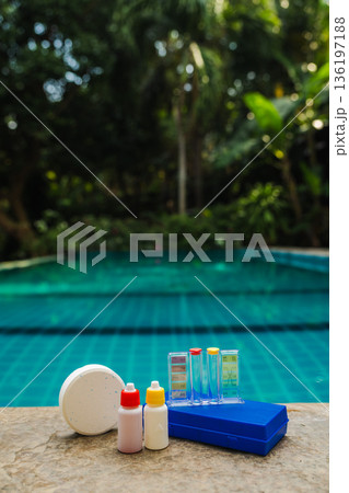Pool water testing kit with chlorine tablet, reagent bottles and color scale on stone edge, tropical pool background Pool water testing kit with chlorine tablet, reagent bottles and color scale on stone edge, tropical pool background 136197188