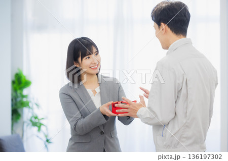 社内で男性にプレゼントを渡す女性 社内で男性にプレゼントを渡す女性 136197302