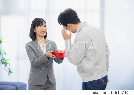 社内で男性にプレゼントを渡す女性 社内で男性にプレゼントを渡す女性 136197305