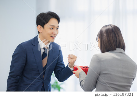 社内で男性にプレゼントを渡す女性 社内で男性にプレゼントを渡す女性 136197321