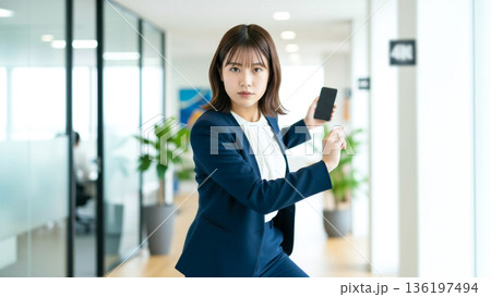 スマホを手に格闘ポーズをとるビジネスウーマン 日本人 スーツ セキュリティ 戦う 強い女性 オフィス スマホを手に格闘ポーズをとるビジネスウーマン 日本人 スーツ セキュリティ 戦う 強い女性 オフィス 136197494