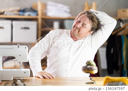 Sitting at workplace, man tailor does limbering-up, warms up numb muscles 136197597