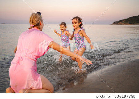 Mother playing with daughters splashing in sea in Greece 136197889