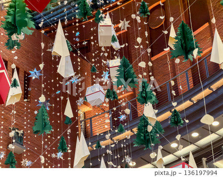 Paper Christmas trees, shimmering stars, and diverse winter ornaments suspended in a grand atrium, evoking festive holiday cheer and seasonal joy Paper Christmas trees, shimmering stars, and diverse winter ornaments suspended in a grand atrium, evoking festive holiday cheer and seasonal joy 136197994