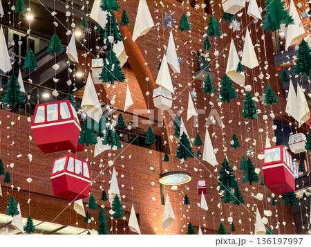 Vibrant red gondola cabins, charming green Christmas trees, and white paper snow suspended as festive winter holiday decorations within a bustling shopping mall atrium 136197997