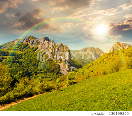 canyon with steep cliffs above the narrow valley at sunset. mountain landscape with unusual land forms in evening light. beautiful springtime scenery. view from the top of a grassy hill under rainbow canyon with steep cliffs above the narrow valley at sunset. mountain landscape with unusual land forms in evening light. beautiful springtime scenery. view from the top of a grassy hill under rainbow 136199890