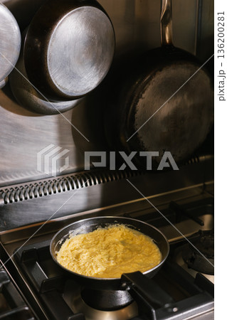 Scrambled eggs cooking in frying pan on stove 136200281