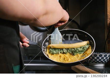 Chef preparing omelet with spinach and cheese filling 136200284