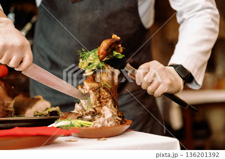 Roast pig with vegetables, gloved chef's hands cut with a knife Roast pig with vegetables, gloved chef's hands cut with a knife 136201392