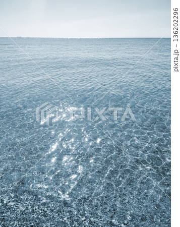Clean transparent water on shallow sandy seashore with shells with shells on sunny summer day. Sun glare on surface of water. Small waves on sea coast. Nature backdrop. Natural background Clean transparent water on shallow sandy seashore with shells with shells on sunny summer day. Sun glare on surface of water. Small waves on sea coast. Nature backdrop. Natural background 136202296