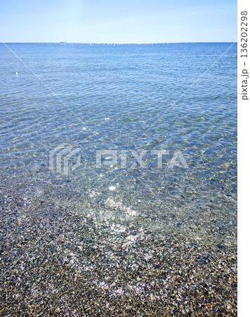 Clean transparent water on shallow sandy seashore with shells with shells on sunny summer day. Sun glare on surface of water. Small waves on sea coast. Nature backdrop. Natural background Clean transparent water on shallow sandy seashore with shells with shells on sunny summer day. Sun glare on surface of water. Small waves on sea coast. Nature backdrop. Natural background 136202298