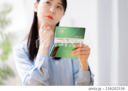 通帳を見て悩む女性 通帳を見て悩む女性 136202536