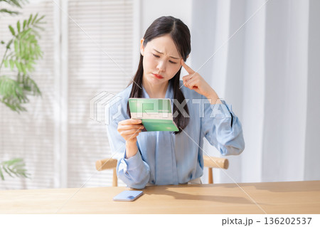 通帳を見て悩む女性 通帳を見て悩む女性 136202537