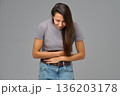 Woman holding stomach and bending forward in discomfort, studio image on grey 136203178