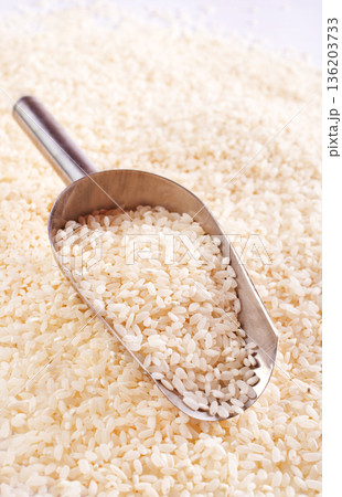 Raw rice spill out of a metal scoop on a light table 136203733