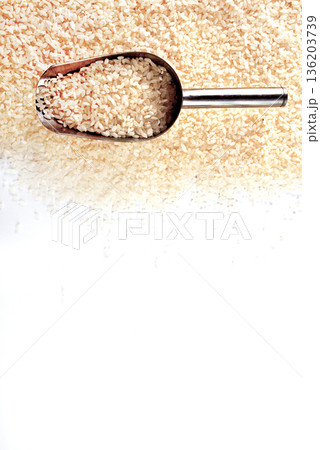 Raw rice spill out of a metal scoop on a light table 136203739