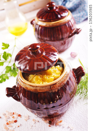 Corn porridge in a clay plate, a clay pot with porridge on a light background Corn porridge in a clay plate, a clay pot with porridge on a light background 136203985